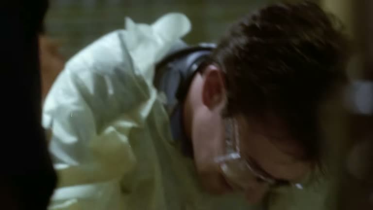 A gowned, goggled physician leans over a trauma patient in the ER